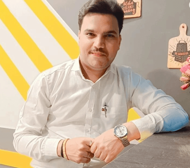 Man in a white shirt leaning on a table with decorative boards in the background.